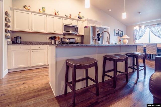 kitchen with lofted ceiling, appliances with stainless steel finishes, wood finished floors, and white cabinetry