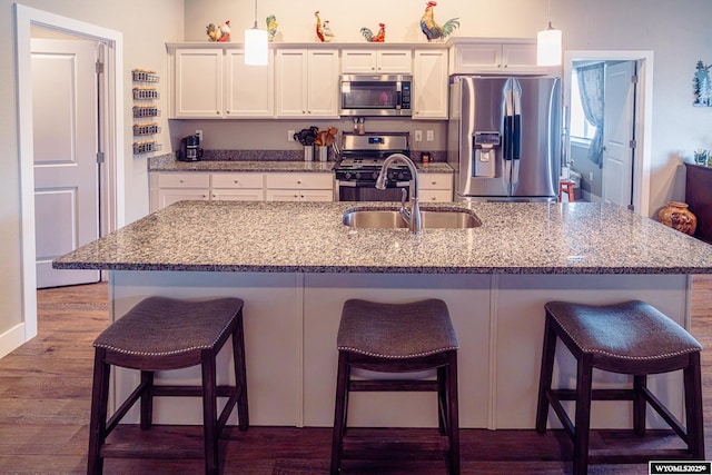 kitchen with stainless steel appliances, dark wood-type flooring, a sink, white cabinetry, and a kitchen bar