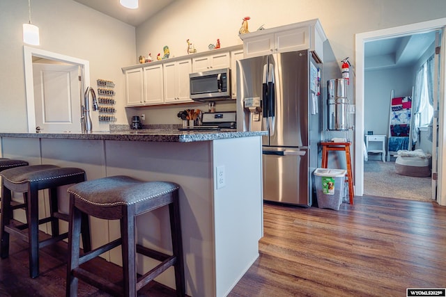 kitchen featuring a kitchen bar, appliances with stainless steel finishes, white cabinets, and dark wood-type flooring