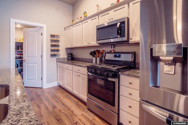 kitchen featuring stainless steel appliances, dark stone countertops, wood finished floors, and white cabinets