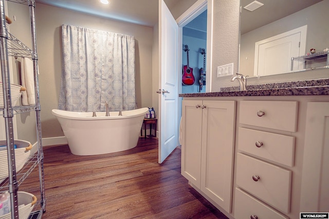 bathroom with a freestanding tub, wood finished floors, vanity, visible vents, and baseboards