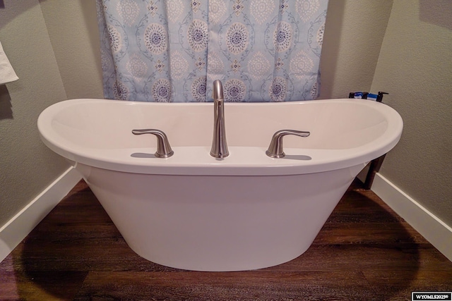 full bathroom featuring baseboards, a textured wall, a freestanding bath, and wood finished floors