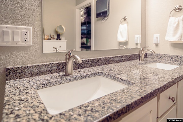 full bath with a textured wall, double vanity, and a sink