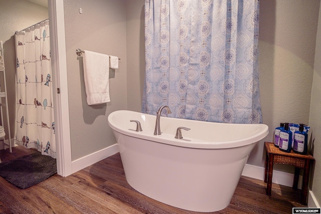 bathroom featuring a freestanding tub, wood finished floors, and baseboards