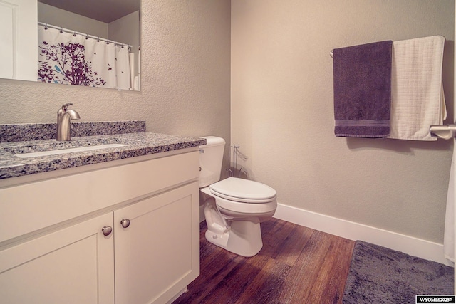 full bath with baseboards, a textured wall, toilet, wood finished floors, and vanity