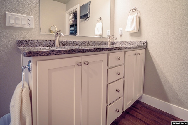 bathroom with double vanity, a textured wall, a sink, wood finished floors, and baseboards