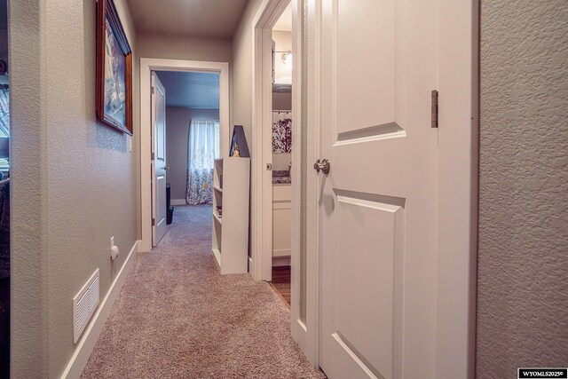 corridor with a textured wall, carpet, visible vents, and baseboards