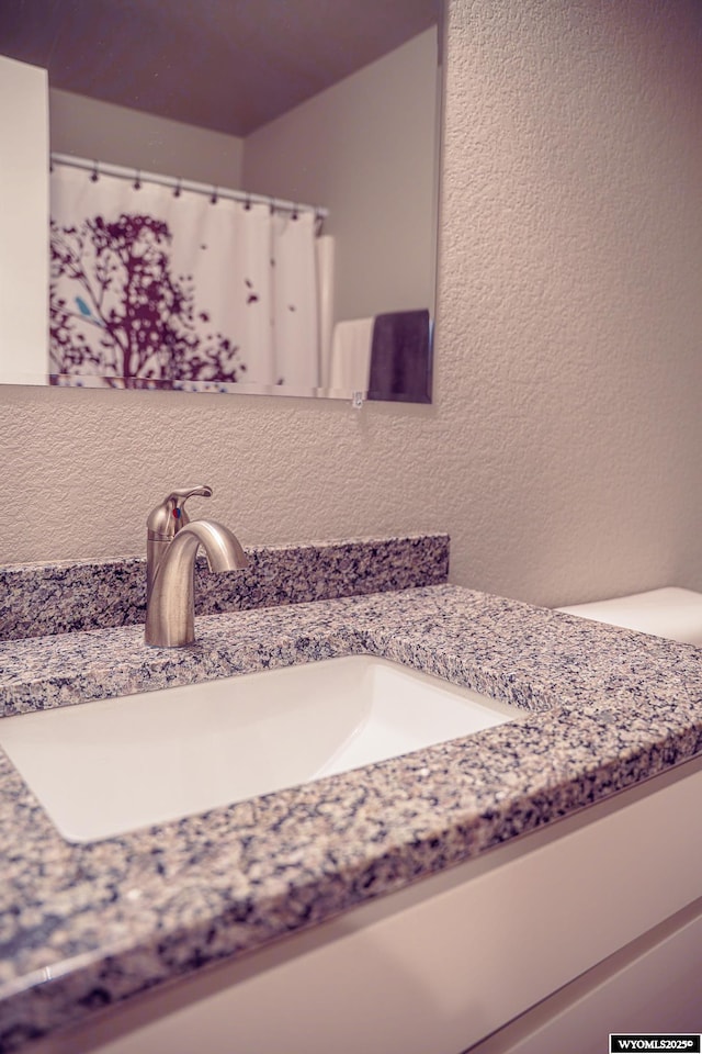 bathroom with a textured wall, a shower with shower curtain, and vanity