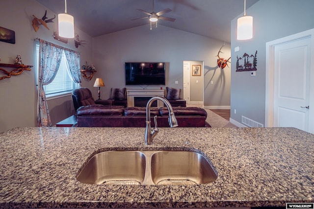 kitchen with visible vents, lofted ceiling, open floor plan, dark stone countertops, and a sink