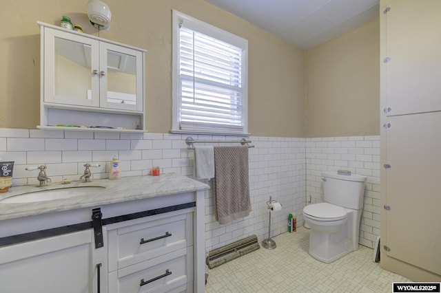 bathroom with tile walls, toilet, wainscoting, vanity, and tile patterned flooring