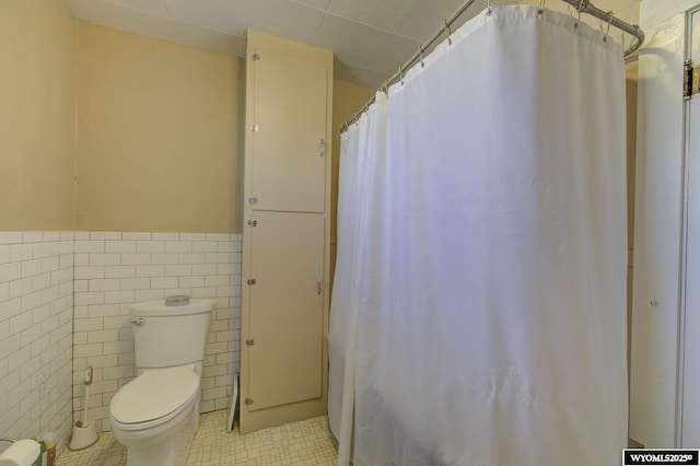 bathroom with toilet, a wainscoted wall, tile patterned flooring, and tile walls