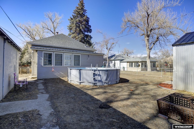 back of house featuring a shingled roof, fence, and an outdoor pool