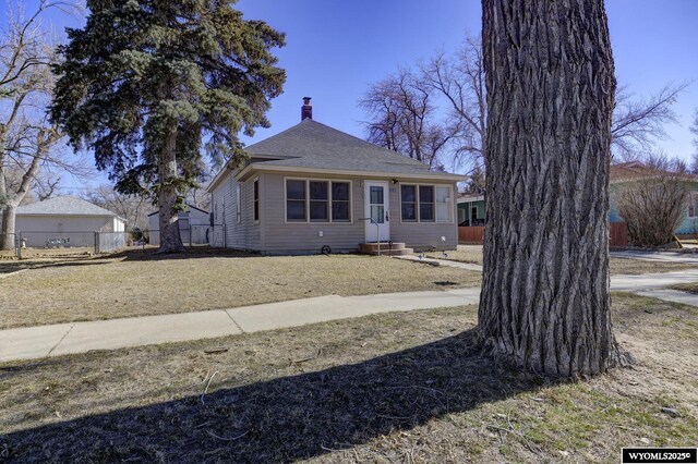 bungalow-style home featuring entry steps, roof with shingles, a chimney, and fence