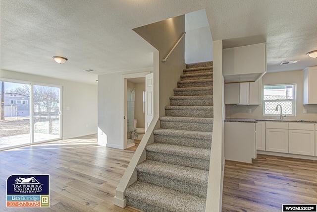 stairs featuring visible vents, a textured ceiling, and wood finished floors