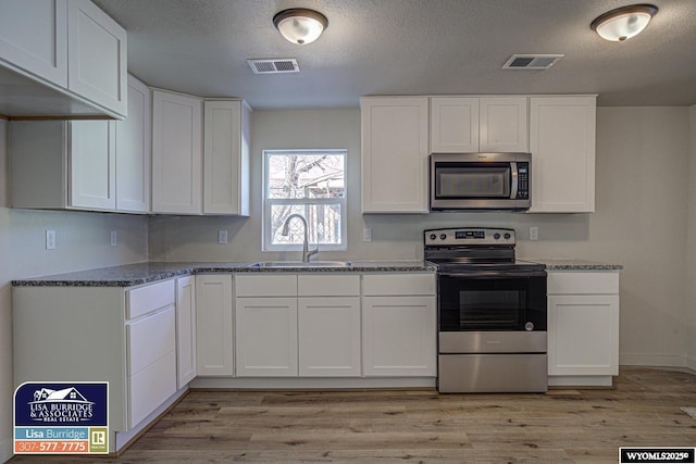 kitchen featuring stainless steel appliances, a sink, visible vents, and light wood-style floors