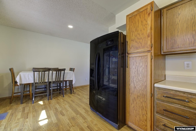 kitchen featuring light wood-style flooring, brown cabinets, light countertops, a textured ceiling, and black fridge