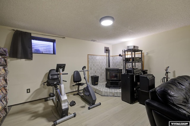 workout room with visible vents, a textured ceiling, light wood-type flooring, and a wood stove