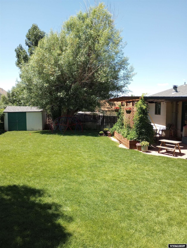 view of yard with a vegetable garden, a storage unit, fence, an outdoor structure, and a patio area