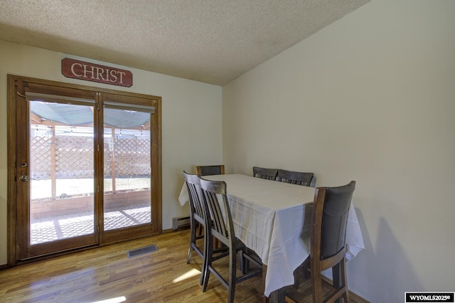 dining area with a baseboard heating unit, visible vents, a textured ceiling, and wood finished floors