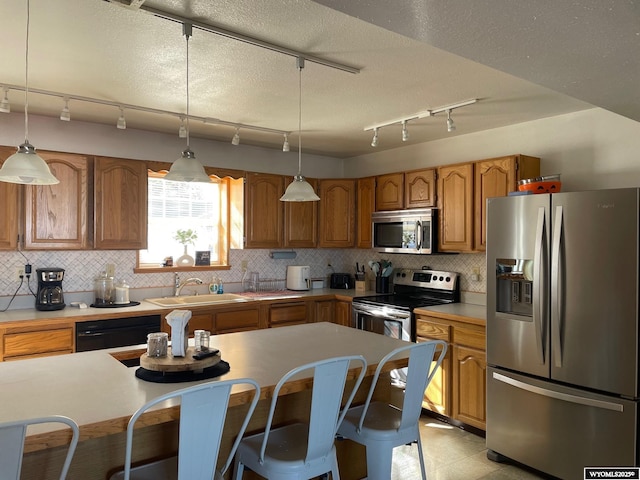 kitchen featuring stainless steel appliances, brown cabinetry, a sink, and decorative light fixtures