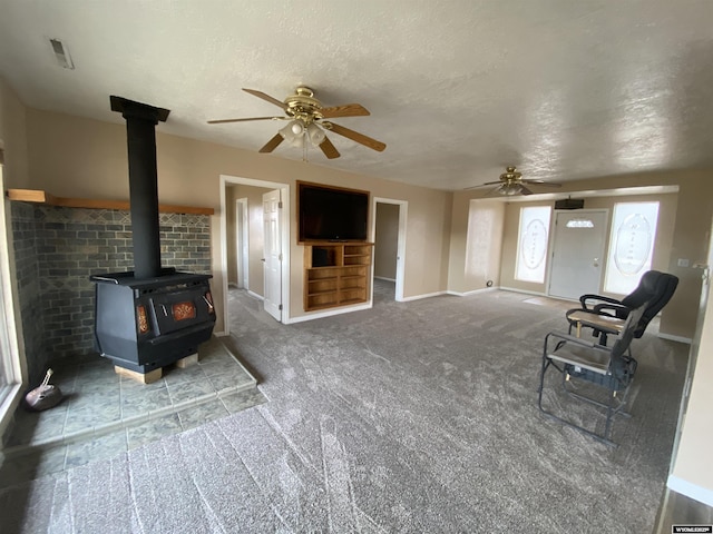 unfurnished living room featuring a wood stove, carpet, ceiling fan, and a textured ceiling