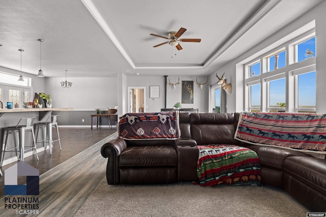 living area featuring wood finished floors, a raised ceiling, a ceiling fan, and a healthy amount of sunlight