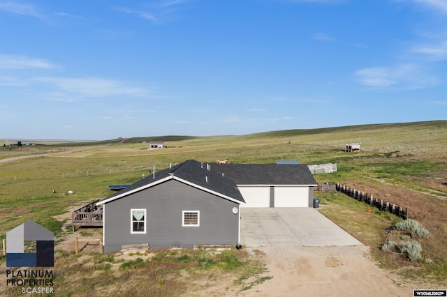 view of front of house with a garage, concrete driveway, and a rural view