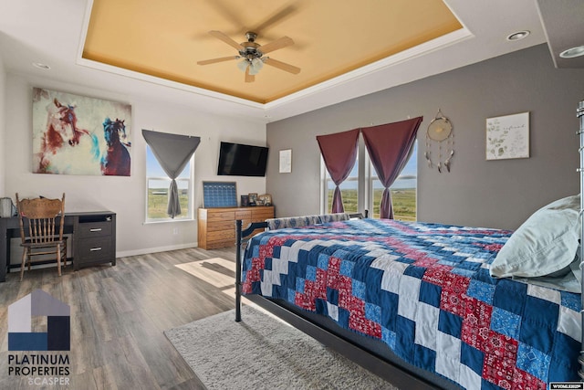 bedroom with a raised ceiling, ceiling fan, baseboards, and wood finished floors