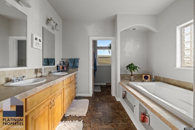 full bathroom featuring double vanity, a garden tub, baseboards, and a sink