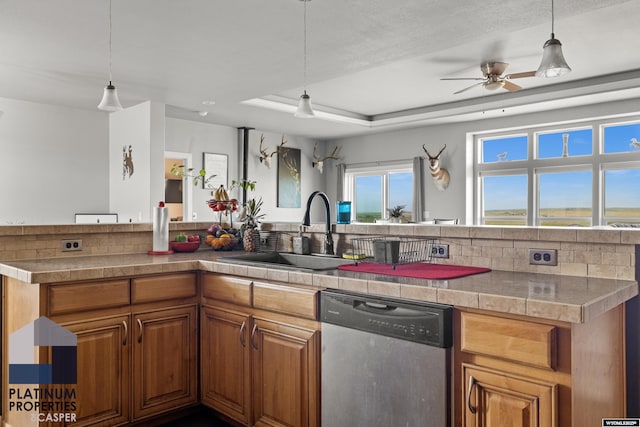 kitchen with a sink, brown cabinets, dishwasher, a raised ceiling, and pendant lighting