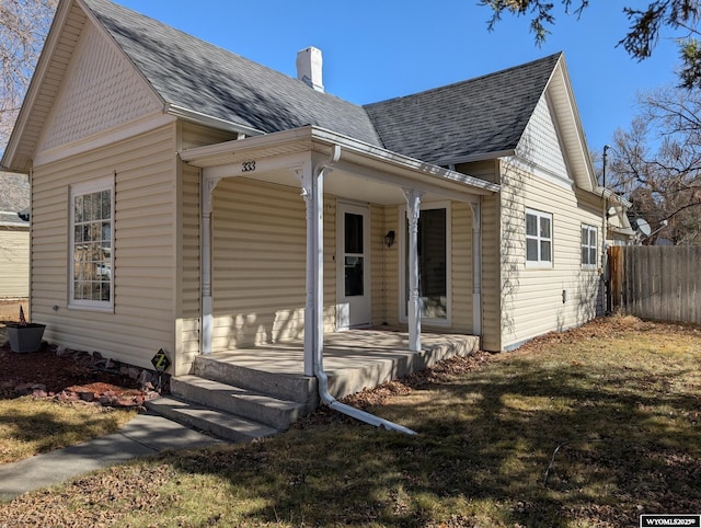 view of front of house featuring a front yard, a chimney, fence, and roof with shingles