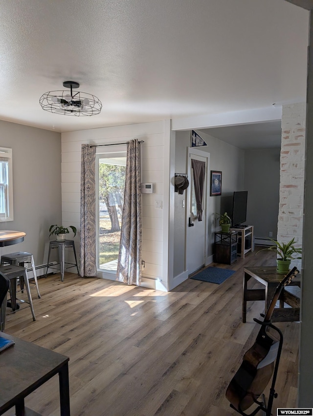 foyer entrance with a textured ceiling, a baseboard heating unit, and wood finished floors