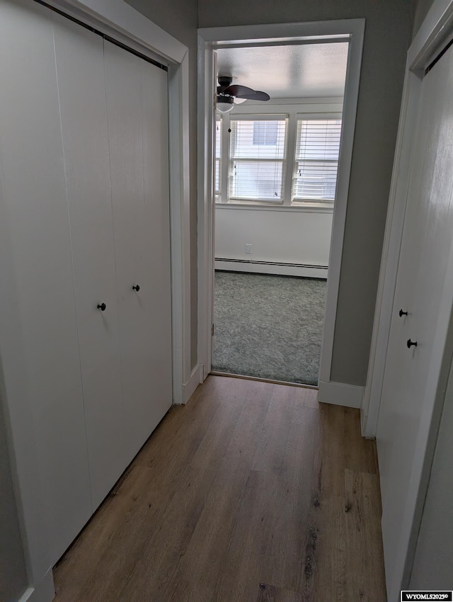 hallway with baseboards, baseboard heating, and wood finished floors