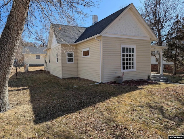 view of side of property featuring a shingled roof, fence, a chimney, and a lawn