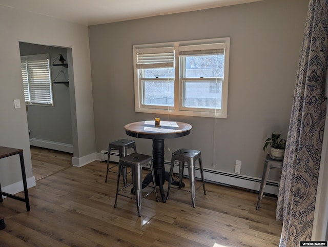 dining space featuring a baseboard heating unit, a baseboard radiator, baseboards, and wood finished floors