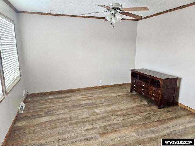 spare room featuring a textured ceiling, wood finished floors, a ceiling fan, baseboards, and ornamental molding