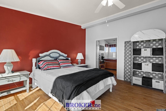 bedroom featuring a ceiling fan, an accent wall, baseboards, and wood finished floors