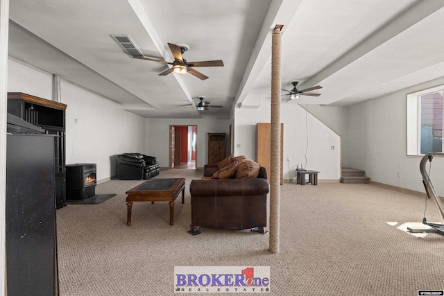 carpeted living area featuring visible vents, stairway, baseboards, ceiling fan, and a wood stove