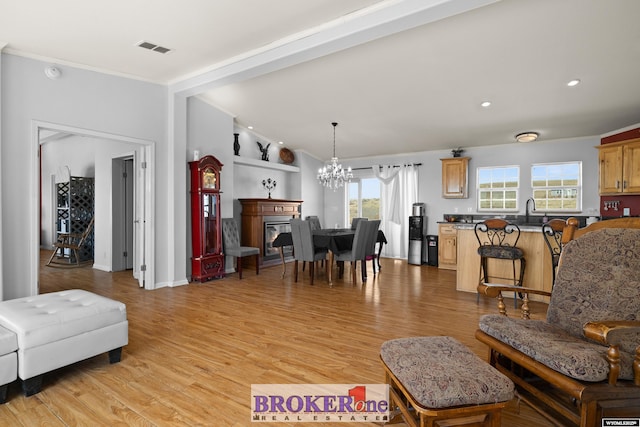 living area with visible vents, lofted ceiling, a glass covered fireplace, light wood-style floors, and a notable chandelier