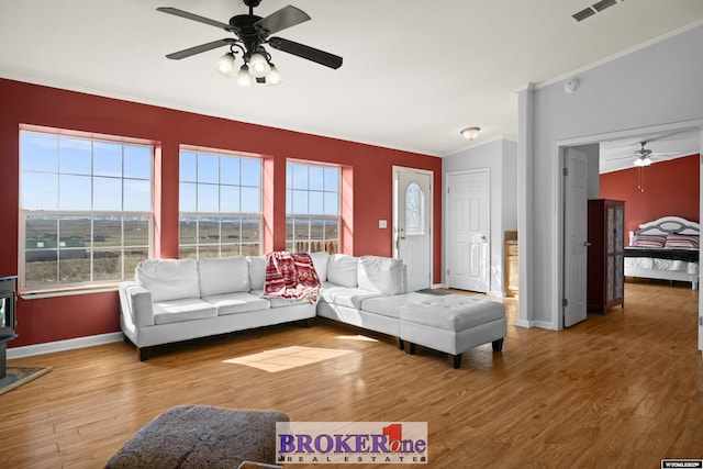 living room featuring visible vents, crown molding, baseboards, a wood stove, and wood finished floors