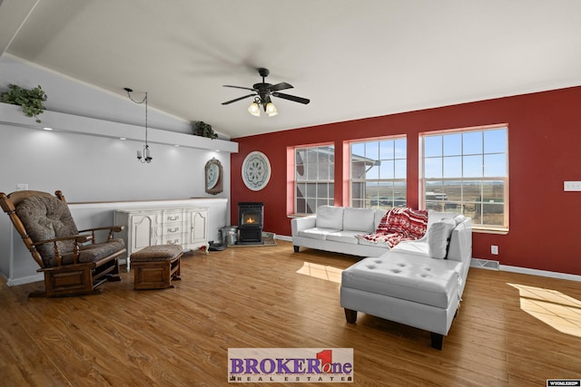 living area featuring visible vents, lofted ceiling, a wood stove, wood finished floors, and a ceiling fan