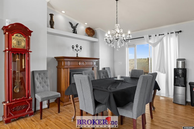 dining area with crown molding, a notable chandelier, a fireplace, and light wood finished floors