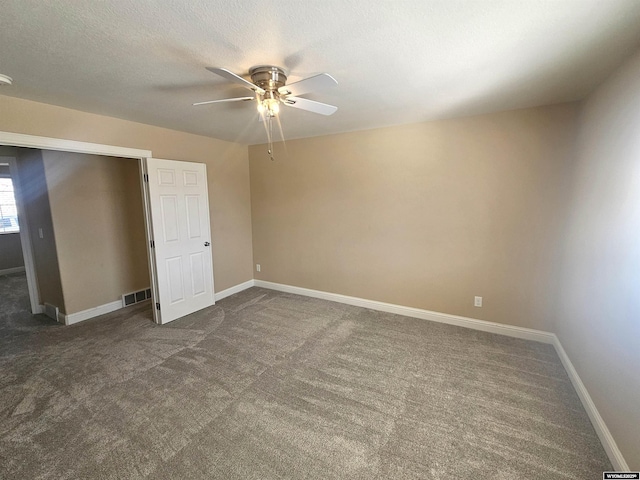 unfurnished bedroom featuring visible vents, dark carpet, a textured ceiling, and baseboards