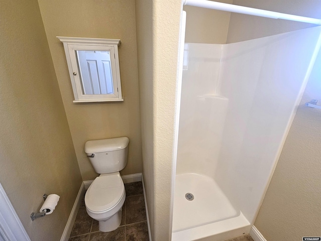 bathroom featuring toilet, a stall shower, baseboards, and tile patterned floors