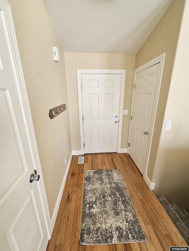 doorway featuring visible vents, vaulted ceiling, a textured ceiling, wood finished floors, and baseboards