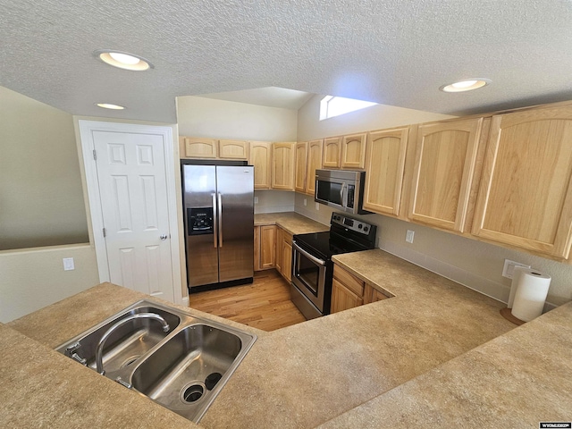 kitchen featuring light wood finished floors, stainless steel appliances, light brown cabinetry, a sink, and a textured ceiling