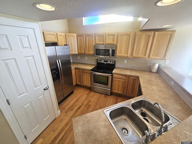 kitchen featuring a textured ceiling, light brown cabinets, a sink, appliances with stainless steel finishes, and light wood finished floors