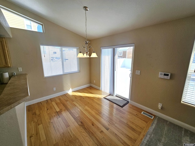 unfurnished dining area featuring a notable chandelier, visible vents, vaulted ceiling, light wood-type flooring, and baseboards