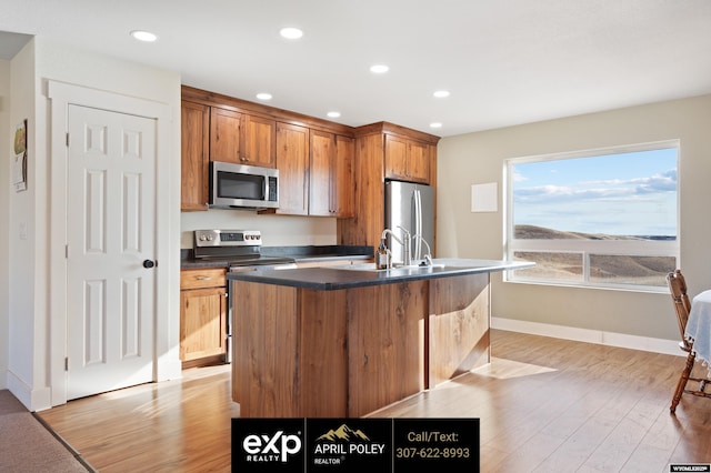 kitchen featuring a center island with sink, stainless steel appliances, dark countertops, recessed lighting, and light wood-style flooring