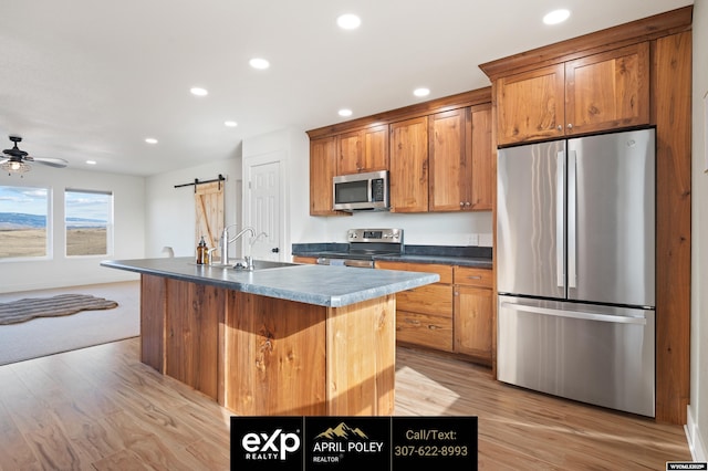 kitchen featuring a barn door, brown cabinetry, dark countertops, stainless steel appliances, and recessed lighting